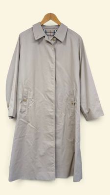 un trench-coat gris suspendu à un cintre devant un mur blanc