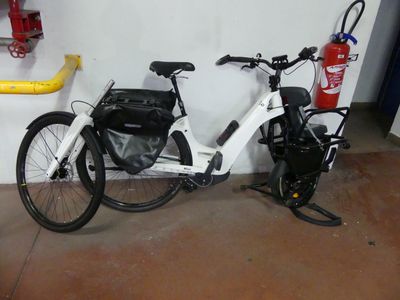 un vélo blanc garé dans un garage, avec un sac à l'arrière