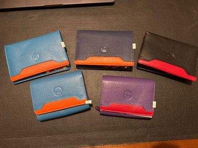 four different colored wallets sitting on a table with a laptop in the background