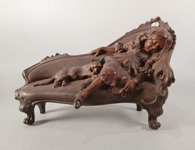 une photo d'une sculpture en bois représentant une femme et un chien allongés sur une chaise longue