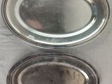 two oval silver trays sitting on top of a metal table