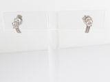 une paire de boucles d'oreilles en argent posée sur un socle en acrylique transparent, sur un fond blanc