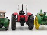 three toy tractors sitting next to each other on a white surface
