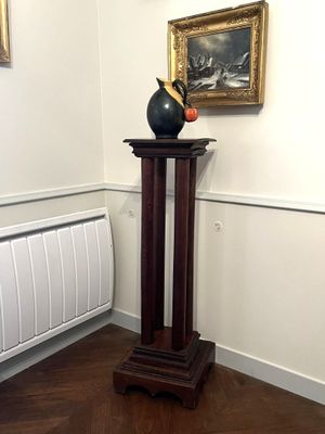 un vase posé sur un socle dans une pièce où se trouve un radiateur