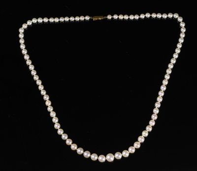 un collier de perles blanches avec un fermoir en or sur fond noir