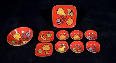a red plate with a bird design on it next to six bowls and a plate with a bird design on it