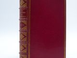 an old red book with gold trim sitting on top of a white surface