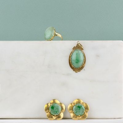 une paire de boucles d'oreilles en or et en jade et une bague posées sur une plaque de marbre