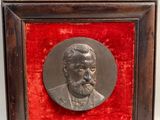 une plaque en bronze représentant un homme barbu, dans un cadre en bois