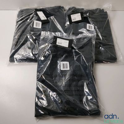 trois t-shirts noirs sont emballés dans des sacs en plastique sur une table