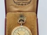 une vieille montre de poche dans une boîte posée sur une surface blanche
