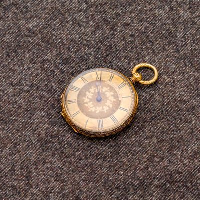 une petite montre de poche en or posée sur un tissu marron