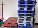 a stack of plastic pallets in a garage next to a stack of blue and red pallets
