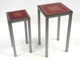 two small metal tables with red glass tops on a white surface