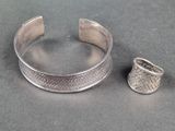 un bracelet et une bague en argent posés sur une table, à côté d'un objet en argent