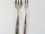 two forks and a spoon on a white surface