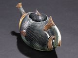a fish shaped teapot sitting on a black surface