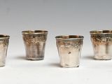 six silver shot glasses lined up in a row on a white surface