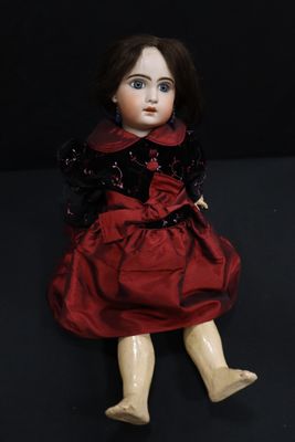 an old doll with a red dress and black shoes sitting on a black surface