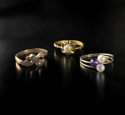 trois bagues différentes ornées de perles, posées sur un fond noir