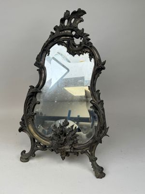 un miroir ancien au motif ouvragé, posé sur un socle, sur fond blanc