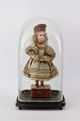 une image représentant une poupée miniature placée dans une cloche en verre posée sur un socle en bois