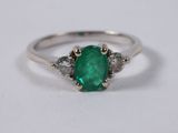 a close up of an emerald and diamond ring on a white surface