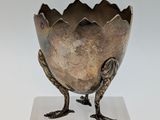 an image of a silver vase with a bird on it ' s feet