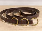 un collier de chien en cuir marron avec des anneaux en laiton posé sur une table en bois