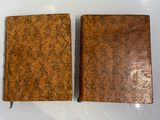 une paire de livres anciens reliés en cuir, posés sur une surface blanche