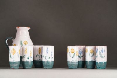 five cups and a jug sitting on a shelf next to each other