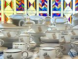 many cups and saucers sitting on a table in front of a stained glass window