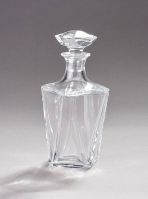 une carafe en verre transparent posée sur une surface blanche, avec une ombre au sol