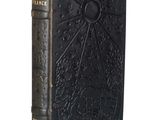 an old book with a black cover sitting on top of a white surface