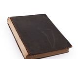 an old book with a black cover sitting on a white surface