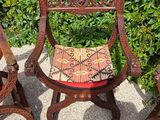 two wooden chairs sitting next to each other in front of a bush