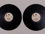 two black vinyl records sitting side by side on a white surface