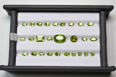 un assortiment de pierres précieuses vertes dans un écrin noir posé sur un fond blanc
