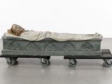 a statue of a man laying on a bed on a dolly