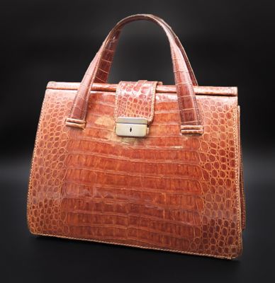 une image représentant un sac à main en peau d'alligator marron sur fond noir