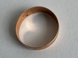 une bague en or posée sur une surface blanche, avec une ombre dessus