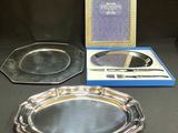 two silver trays and a mirror on a table next to a picture frame