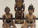 trois statues en bois représentant des personnes assises sur une surface blanche