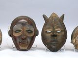 Quatre masques africains sont exposés sur des socles en acrylique posés sur une surface blanche.