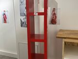 a tall red bookcase in the corner of a room with pictures on the wall