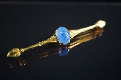 une image représentant une broche en pierre dorée et bleue posée sur une surface noire