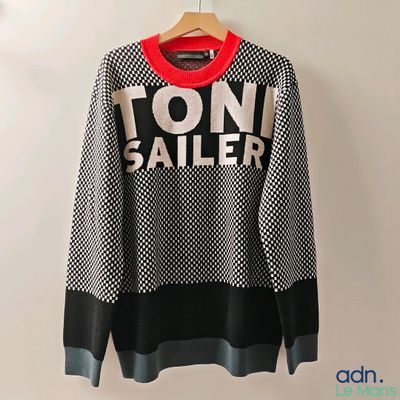 un pull noir et blanc avec un col rouge, suspendu à un cintre