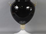 a black vase with gold handles on a white pedestal