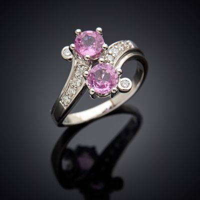 une bague sertie d'un saphir rose et de diamants, posée sur un fond noir