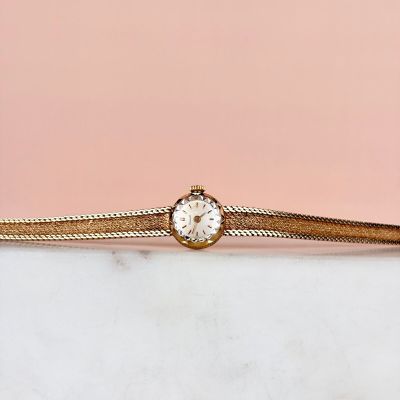 un bracelet en or sur lequel est fixée une montre, posé sur une surface en marbre